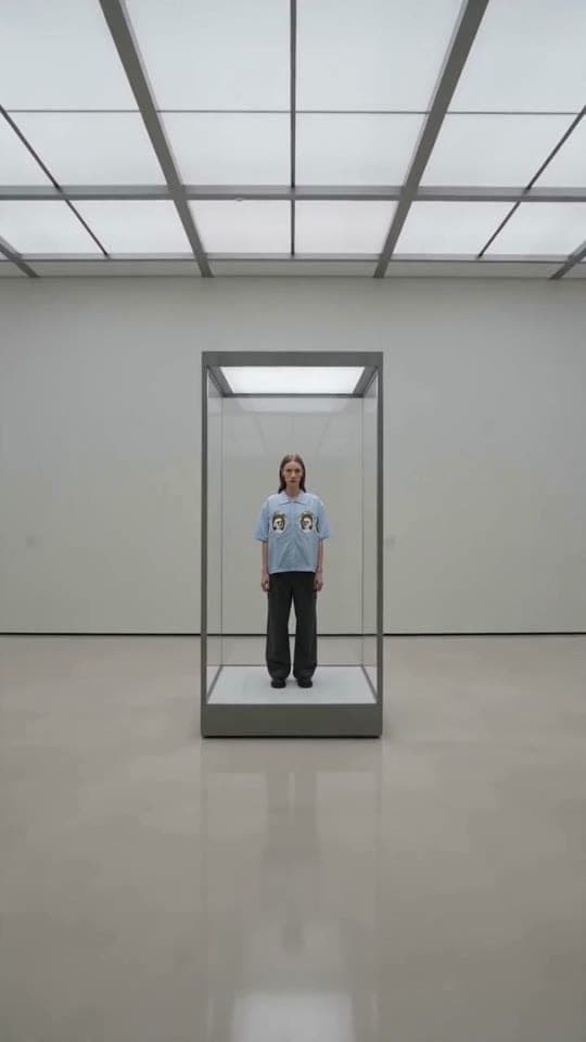 The camera glides through a stark gallery and finds oxkyy displayed inside a glass vitrine like living art.