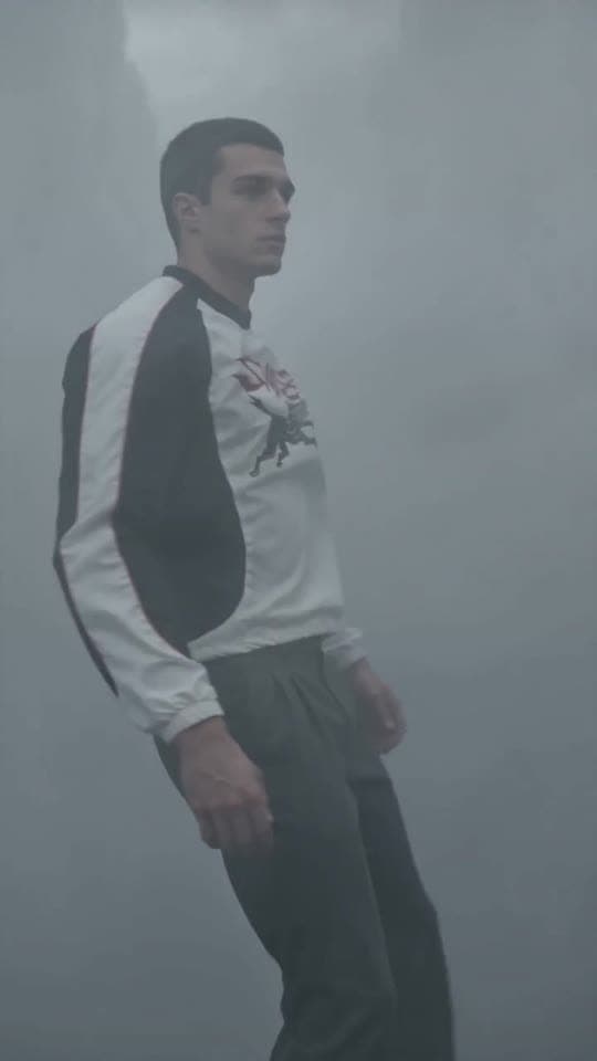 ezzel floats upright in a vast storm-grey void, unbothered, the look glowing against the grey.